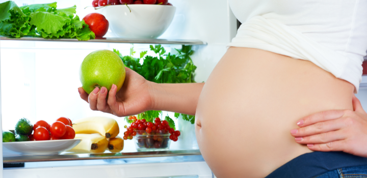 Pregnant woman holding an apple, providing guidance on what to avoid during pregnancy